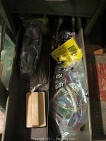 View of one drawer with tape measure in bag, screws, nails, and bungee cords in plastic bags.