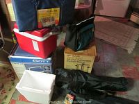 Multiple camping and picnic items including soft sided cooler bags, hard cooler boxes, styrofoam cooler, camping chairs, and boxed coffee maker all displayed together.