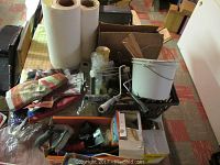 Wide view of box contents showing paint rollers, stir sticks, light bulbs, flags, and other items on a table.