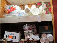 Wide shelf with various disposable party items including paper plates, styrofoam bowls, napkins, plastic cups and a wicker basket.
