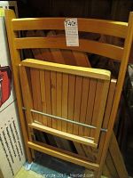 Photo shows one wooden folding chair in folded position highlighting the slatted backrest and seat.