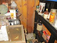 Wide view showing barware, glass pitchers, tins, mug, and various items on wooden shelves and a wooden table with inlaid design.