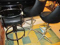 Three black vinyl and metal bar stools with star-shaped metal bases and triangular footrests, arranged on floor near stairs.