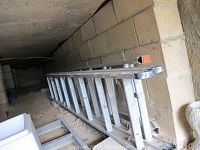 Image showing two telescoping metal ladders lying side by side on a dirt floor against a brick wall, exhibiting paint spots and dirt.