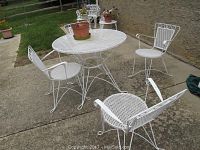 White metal patio table and four matching white metal patio chairs around the table on a concrete patio, one flower pot on the table.