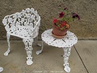 Photo showing the white cast iron chair and matching table side by side with a flower pot on the table.