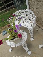 White cast iron garden bench and matching table on a patio, showing grapevine and leaf decorative pattern.