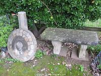 Cement garden bench and stone birdbath resting on ground under bushes.