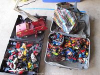 Overview of Tonka crane truck alongside open suitcase and trays filled with assorted toys including Transformers and Voltron parts