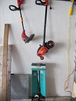 Photo of three outdoor power tools hanging on wall: Black & Decker Hedgehog, Homelite weed eater, Ryobi Trimmer Plus in original box at bottom
