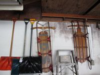 Photo showing three snow shovels of different styles and two vintage wooden sleds hung on a wall.