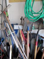 Yard tools including rakes, shovels, hoe, showing details of wooden handles and metal heads with rust.