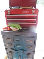 Shows the red Craftsman tool chest stacked on top of the gray VanDorn Steel chest, a pair of gloves and some small items placed on the metal surface between chests