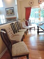View of all six dining chairs lined up along a wall and window with hardwood floor, showing four wood frame chairs with upholstery and two tufted arm chairs.