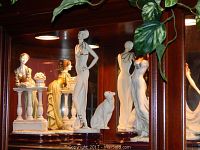 Three figurines displayed side by side in glass cabinet with foliage overhead