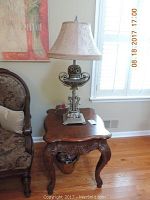 Side view of the ornate wood side table with cabriole legs and decorative lamp on top, showing the carved scrollwork on the table apron and lamp base.