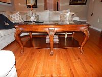 Coffee table with carved legs and glass top, hardwood floor background