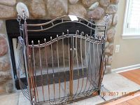 Front view of the silvertone metal fireplace fence with vertical bars and curved decorative top placed in front of a stone fireplace.