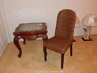 Wooden accent table with glass and metal decorative inset next to wicker covered chair with wooden legs.