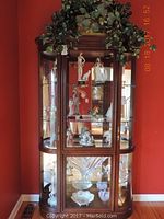 Front view of dark wood curio cabinet with artificial plant on top
