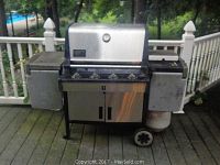 Full view of Weber Summit Silver gas grill with attached gas canister, showing side trays and wheels.