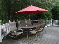 Patio set with oval table, six cushioned chairs including two swivel chairs, and large red umbrella on outdoor deck.