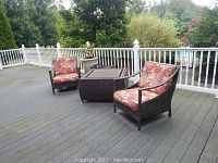 Two wicker chairs flanking square wicker table on deck with planter behind