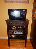 Microwave oven placed on hand-painted wooden table with floral and butterfly designs, showing overall lot.