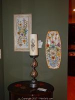 Two framed floral pictures hung on wall with a decorative candle holder lamp placed on a small table beneath them, showing size and style of each.