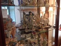 Multiple decorative porcelain and crystal figurines displayed on glass shelves