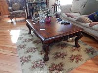 Wood coffee table shown in a living room setting on floral rug; claw feet and carved apron detail visible