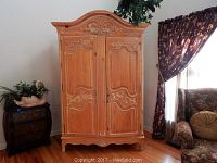 Front view of the wooden Italian style armoire showing carved door panels, decorative crown and lower apron details.