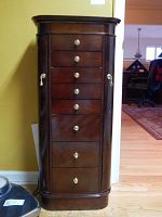 Front view of the dark wood jewelry armoire showing the eight drawers with brass knobs and smooth polished finish.