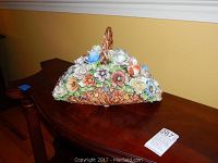 Porcelain flower basket by B Bonalberti featuring colorful gros relief flowers arranged in a basket with handle, placed on a wooden surface.