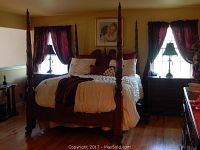 Front view of carved wood poster bed with headboard, footboard, turned posts and bedding between two windows