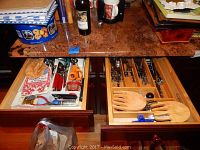 Overview of two open kitchen drawers displaying organized stainless steel flatware and wooden salad servers along with other utensils.