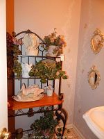 Full view of bakers rack with several decorative items placed on shelves in a bathroom setting near pedestal sink