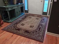 Floral patterned area rug with cream center and burgundy border on hardwood floors by entrance door.