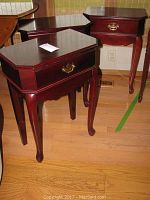 Three reddish-brown wooden side tables with curved legs and brass drawer handles shown together on hardwood floor.