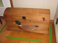 Front view of the wooden chest showcasing the hand-carved and painted Mallard duck detail on the front panel, curved lid, and metal handle latch.