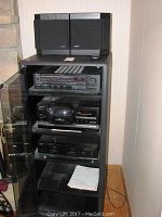 Stereo cabinet with glass door open showing stacked stereo components and Bose speakers on top.