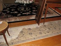 Photo showing large black floral area rug and cream runner rug partially under furniture on hardwood floor.