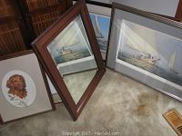 Photo showing the beveled mirror with wood frame leaning against framed prints including sailboat and dog portrait.