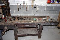 Wide view of wooden workbench with multiple hand planers, chisels, brushes, and other small woodworking tools arranged on top and some hung on pegboard behind