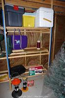 Full view of the camping items including coolers, stoves, lanterns, bags on the shelf in a garage or storage area.