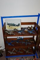 Wooden three-tier shelf holding multiple model airplanes and aircraft-related posters and pictures