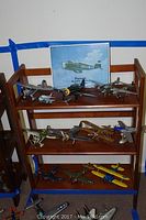 Wood wooden shelf holding multiple model airplanes arranged across three shelves, various sizes and styles including military and civilian designs.