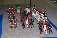 Wide angled view of all six horse-drawn cast iron vehicles and horses in the lot arranged on floor.