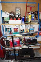 Shelf with assorted car cleaning supplies including bottles of wax, cleaners, brushes, and equipment like the Waxmaster 900 waxer and 50 amp booster cables.