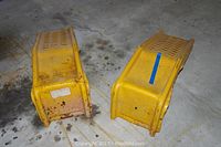 Two yellow metal car ramps placed side by side on concrete floor with visible rust and dirt.
